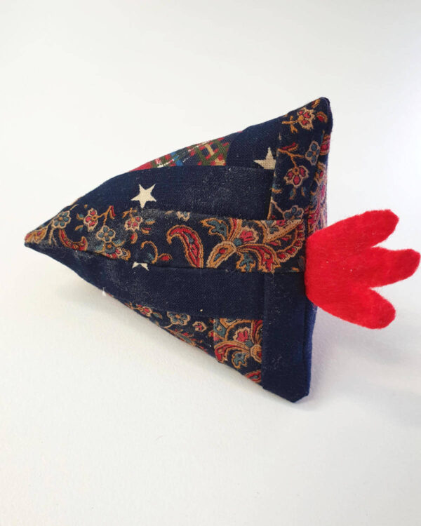 Handmade pin cushion chicken featuring a red felt comb, wrapped in paisley and star-patterned fabric reminiscent of log cabin quilt blocks, placed on a white surface.